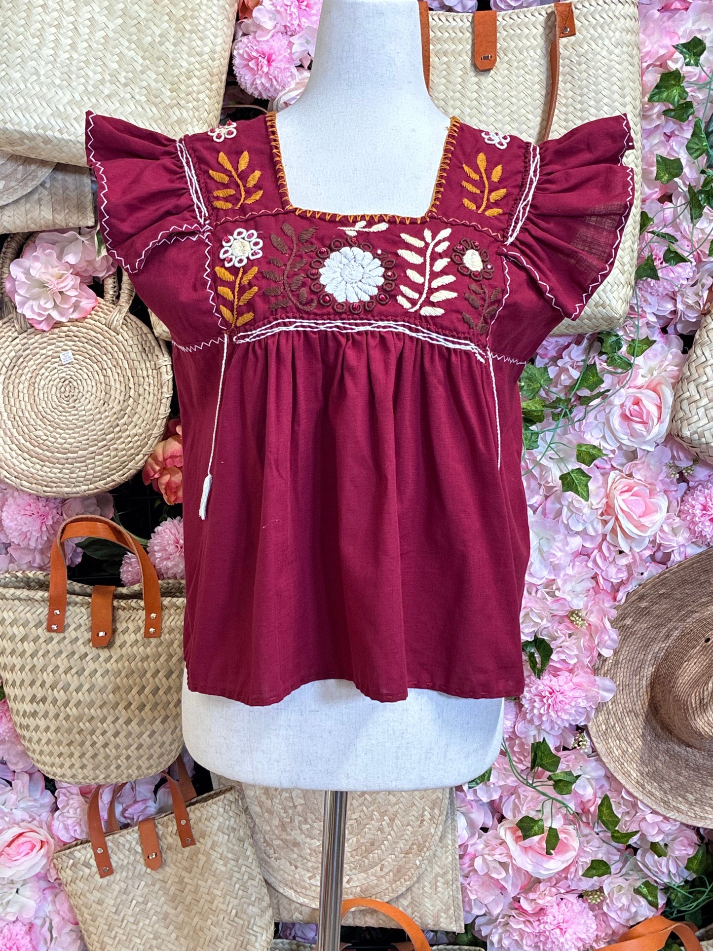 Detalle del bordado rococó con flores en crema y dorado con cristales rojos en blusa guinda